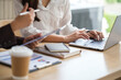 © wattana - Close-up of hands working on laptop and tablet during a business discussion at a modern desk.