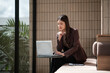 © wattana - Focused businesswoman analyzing data on her laptop in a bright, modern setting.