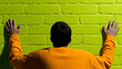 © SashaMagic - Person leaning on a bright green brick wall, wearing orange.