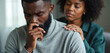 © miss irine - Black man sitting with closed eyes, hand on chin, looking sad. Woman comforts him, hand on shoulder, eyes closed. Man stressed, woman showing empathy and support. Couple in emotional moment together.