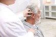 © New Africa - Doctor putting hearing aid into senior man's ear in hospital, closeup