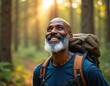 © miss irine - Senior Black man with backpack hikes in green forest. Smiles, looks up at golden sunlight through tall trees. Happy old guy enjoys nature walk, outdoor sport, healthy lifestyle. Adventure travel,