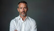 © miss irine - Middle aged man with gray beard wears white shirt. Looks directly at camera in studio. Confident male adult stands against dark gray background. Pro business person portrait, serious expression for