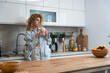 © Srdjan - Sleepy young woman in home kitchen sipping coffee slow morning routine in casual loungewear, striped shirt and messy curls, enjoying a quiet break by the counter before starting the day