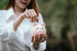 © Worawi - A woman wearing a white shirt is saving money by putting a coin into a pink piggy bank, symbolizing financial planning and saving for the future.