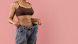 © Anastasiya - Cropped image of toned woman in brown underwear holding oversized jeans. Symbol of significant weight loss, fitness goal achievement, and healthy lifestyle transformation, copy space