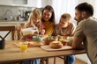 © Goran - Happy little girl pouring milk into bowl of cereals while eating breakfast with her family at dining table.