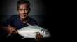 © Kitta Studio - Elderly Fisherman Holding Fresh Fish Against Dark Background