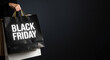 © TAMER YILMAZ - Shopping bags with “Black Friday” written on them, held by a hand against a black background. Copy area.