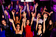© deagreez - Energetic party scene with smiling dancers raising hands in a neon lit club crowd during a lively celebration