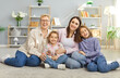 © Studio Romantic - Portrait of a happy family with grandmother, mother, and two children sitting together on the floor at home living room, showcasing love and affection, bonding and warm relationship dynamics.