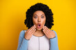 © deagreez - Surprised young woman with curly black hair against a vibrant yellow background displaying an astonished facial expression