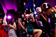 © deagreez - Energetic festive party scene with friends dancing in a nightclub wearing Santa hats and glamorous outfits as bright neon lights glow