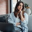 © Daniel - Distracted from work worried young woman sitting on couch with laptop, thinking of problems. Pensive unmotivated lady looking at window, feeling lack of energy, doing remote freelance tasks at home.