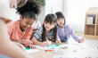 © paulaphoto - Group of happy, multicultural kids lying on floor and doing colorful drawings with crayons during creative indoor school activity.