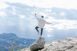 © Анна Демидова - A man stands on one leg on a rock high in the mountains. A young woman in a white hoodie and black jeans looks down at the city and the sea. A magnificent view of beautiful nature.