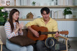 © itchaznong - Musical Moment. A young couple enjoying a guitar session together in a cozy living room.