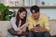 © itchaznong - Joyful couple sharing a moment while using smartphones indoors