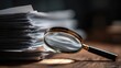 © Pavel - Detailed view of a stack of important documents with a magnifying glass on a wooden table in a dimly lit room