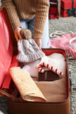 Woman packing warm clothes, passport and Christmas decor into suitcase at home, closeup