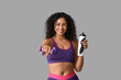 © Pixel-Shot - Sporty young African-American female coach with water bottle and dumbbells on white background
