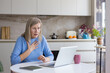 © Liubomir - Senior woman suffering from sudden pain or anxiety, touching her chest and looking worriedly at the laptop screen during a virtual conversation in her kitchen