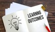 © Danish - learning outcomes, white paper, lightbulb, wooden background, business documents