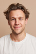 © MYKHAILO KUSHEI - A young adult man smiles warmly at the camera. He has medium brown hair and blue eyes. He is wearing a plain white t-shirt. The background is a neutral color.