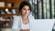 © Ilja - Dark-haired woman smiling and focused while working on her laptop in a bright personal office.
