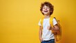 © miss irine - Happy schoolboy with curly hair laughs showing thumbs up sign. Cute kid with yellow backpack smiles on studio background. Cheerful child expresses joy success, fun going to school. Smiling student