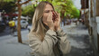 © Krakenimages.com - Woman cups both hands around mouth shouting on street amid blurred trees and parked cars under bright daylight; alert communication announcement attention.