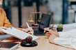 © Kritdanai - Legal Consultation: Two professionals sit at a desk, carefully reviewing and signing legal documents. In the background a scale of justice rests, and a gavel sits nearby.