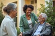 © miss irine - Young African American woman visits elderly father in wheelchair. Smiles, talks with dad. Another senior woman joins happy family conversation outdoors at care home. Multi generational bond. Diverse