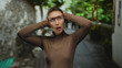 © Krakenimages.com - Young woman with glasses covering her ears stands outdoors on a city street, reacting to loud noise and looking around with concern.