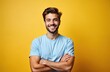 © Pete - Handsome bearded man poses in studio against yellow background. Brunette guy smiles with crossed arms. Male model in casual light blue tshirt. Successful hipster person looks at camera shows