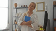 © Krakenimages.com - Woman with blonde hair tied back holding tablet smiles softly in studio surrounded by ceramic pots and shelving; contentment.