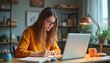 © Pete - Young woman studies at desk with laptop, notebook. Female student writes notes, uses computer for research in cozy home office with warm lamp light. Prepares for exams, homework in organized