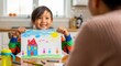 © Katlyn Design - Young boy proudly displaying his colorful crayon drawing of a house family and sunny sky indoors