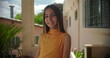 © Marco - Close-up portrait of a smiling young girl on a Latin American balcony with pastel buildings and greenery in the background, cheerful and confident expression