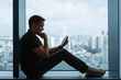 © kieferpix - Man Sitting by Window Looking at Smartphone – Thinking, Messaging, and Reflection