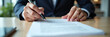 © AlenaSi - Signing contract on desk in office, man holding pen in hand above document. Signing contract involves reading agreement and details. Concept signing contract for legal terms.