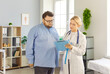 © Studio Romantic - Patient and doctor consultation in medical clinic. Overweight fat man listens as female physician reviews notes, discusses obesity risks and treatment. Healthcare guidance and support concept.