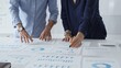 © rogerphoto - Professional team reviewing financial documents, pointing at charts on desk, collaborating to analyze data and strategize business growth. Business people concept