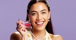 © peopleimages.com - Portrait, makeup and woman with lip gloss choice for color variety, options or advertising in studio. Smile, cosmetics or model with lipstick product for gen z beauty, hydration and purple background