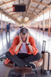 © Tj - Traveler experiencing frustration, stress, and anxiety from a delayed journey, sitting on a waiting bench with luggage at a busy train station platform