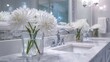 © JovialFox - Elegant white anemone flowers in a clear glass vase on a modern white marble bathroom vanity with chrome faucets and sinks