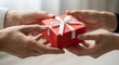 © Imam - Hands exchanging a red gift box with white ribbon.