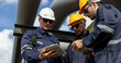 © eakgrungenerd - Engineer wearing safety gear using digital tablets at an industrial facility, discussing data and operations under large pipelines, symbolizing technology integration in modern engineering.