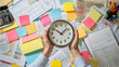 © tynza - Person holding a clock above a messy office desk covered with colorful sticky notes, documents, and charts, symbolizing stress and time management