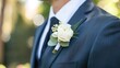 © ds17 - Close-up of a white rose boutonniere with greenery pinned on a dark blue suit jacket at a formal event.
